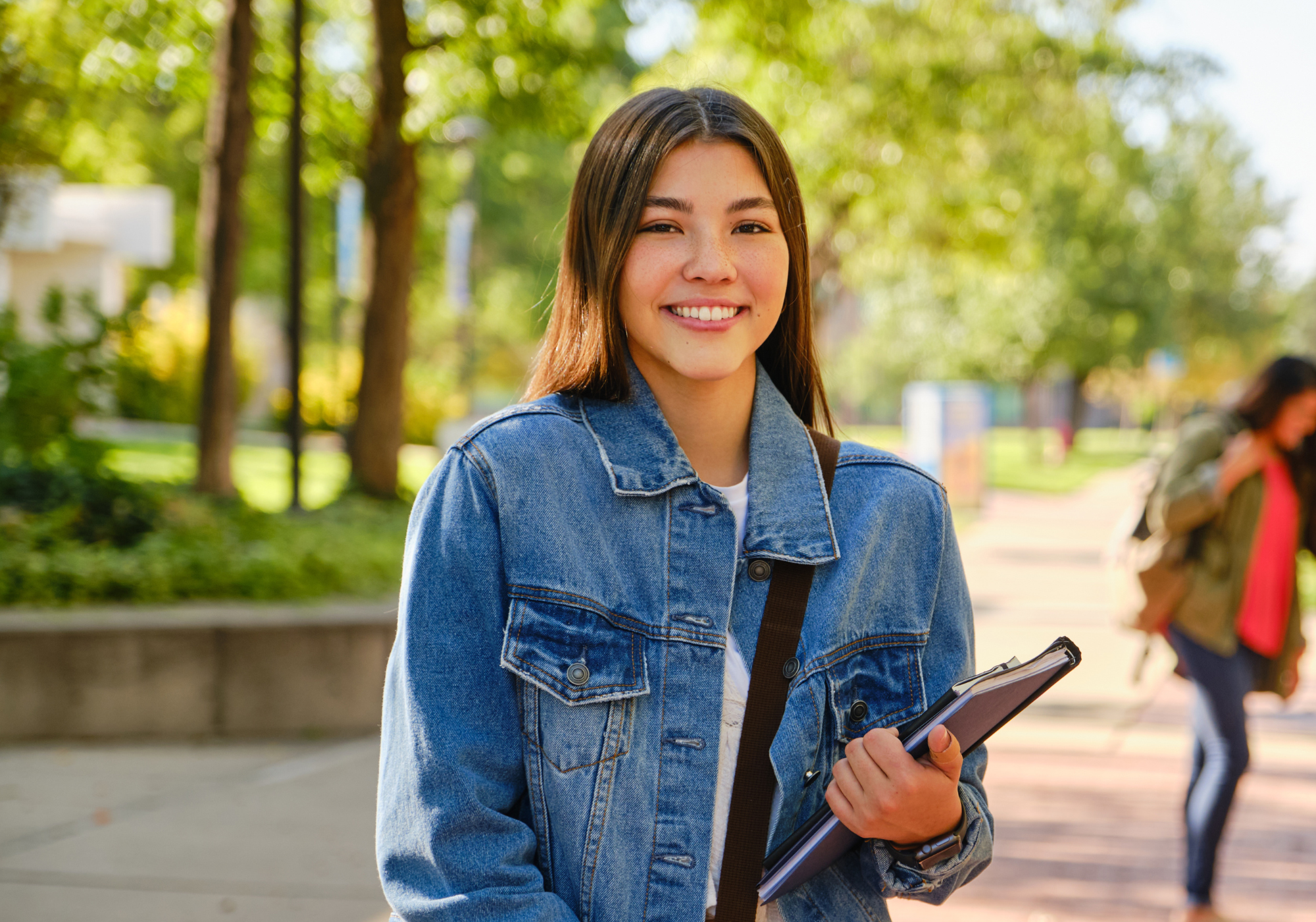 College student on campus smiling while holding a notebook